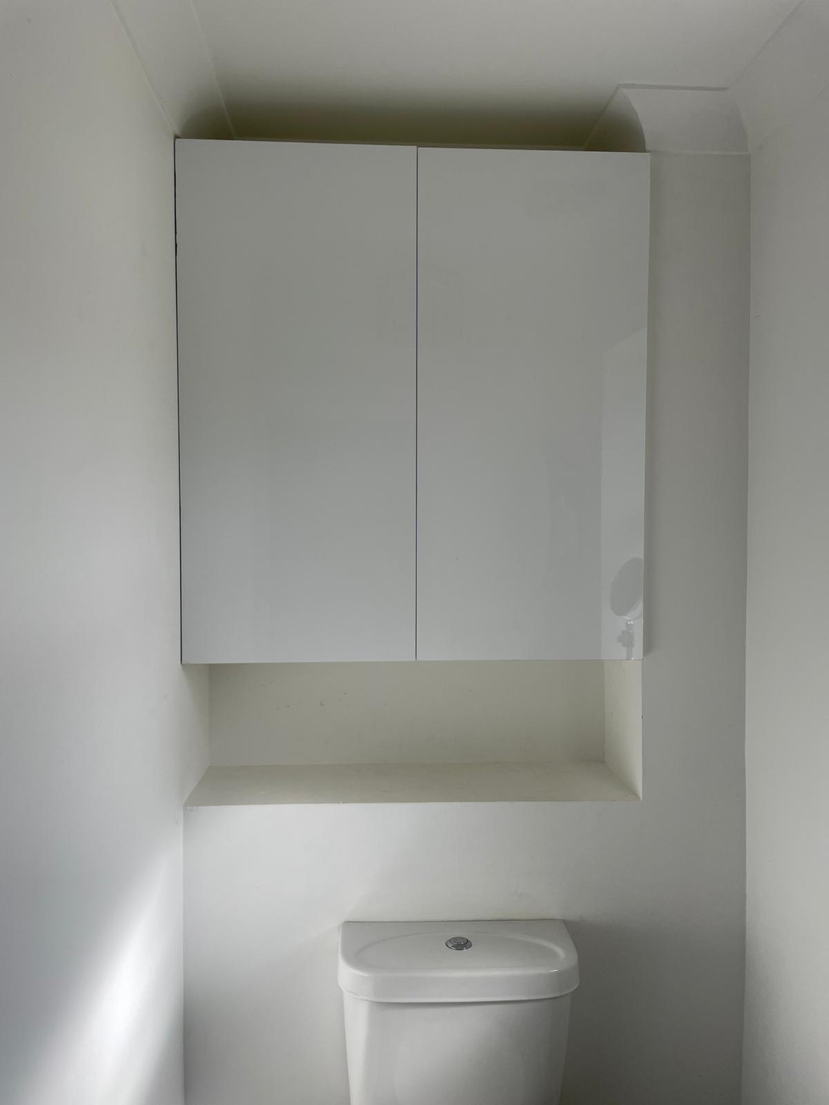 Finished white storage cupboard fitted above a toilet